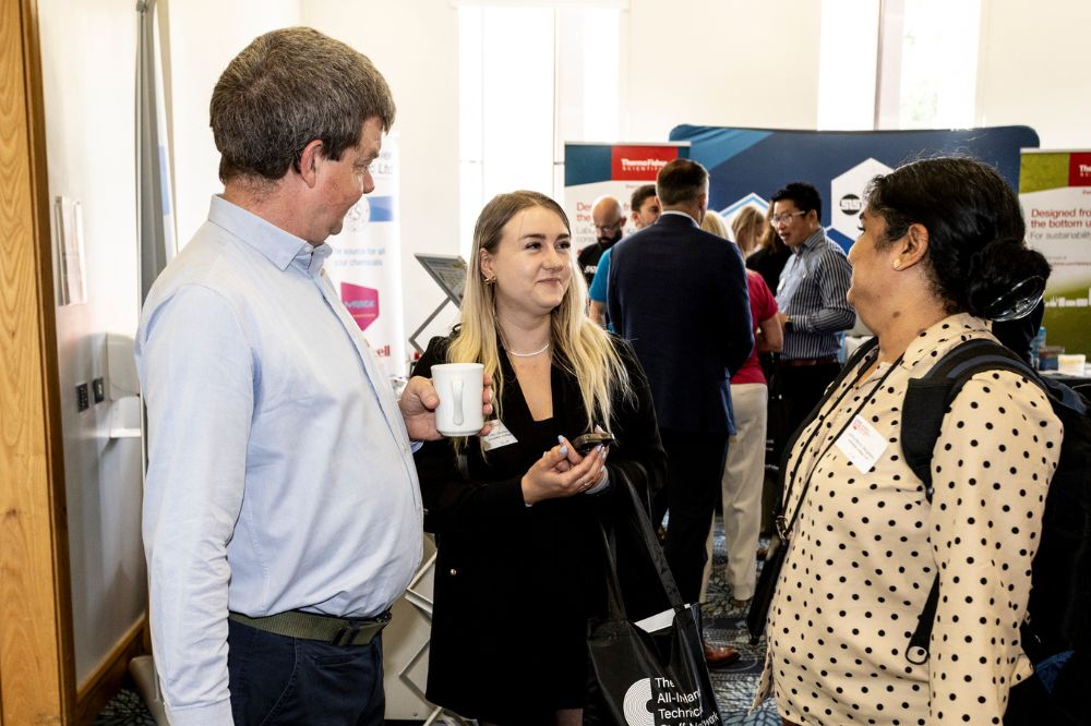 Two females and one male stadning talking in an exhibition setting facing each other in an open circle arrangement